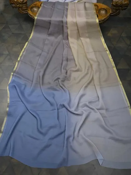 A modern ombre-dyed chiffon saree in shades of grey and blue with a thin gold border. This is a chic and understated piece for a contemporary party look.