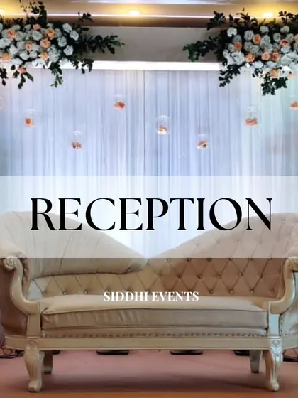 A classic reception stage setup featuring an elegant chaise lounge, a backdrop of peach and white florals, and delicate hanging glass terrariums.