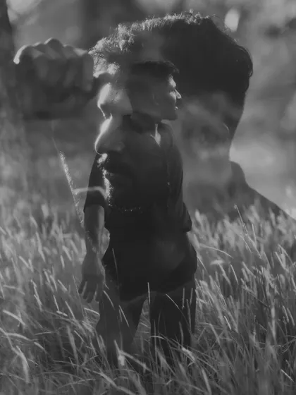 An artistic double exposure portrait in black and white. This conceptual image layers two perspectives of a man in a field of tall grass, creating a thoughtful and surreal visual narrative.