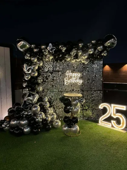 This outdoor rooftop setup for a 25th birthday demonstrates how I can transform any space. It features a black and silver theme with a large shimmer wall, a neon sign, and marquee numbers, creating a stylish party atmosphere.