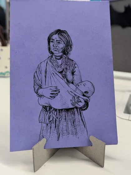 A simple yet powerful ink illustration titled "Amma," capturing the universal bond between a mother and her child. The drawing is displayed on a small stand, showing how even small art can make a big impact.