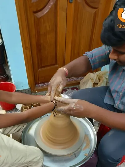 An instructor guides a student's hands on the spinning pottery wheel, helping him feel the motion and pressure needed to shape the clay.