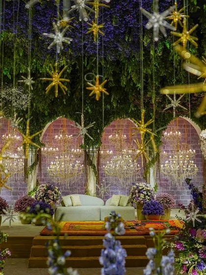 A full view of the stage, with its canopy of greenery, hanging stars, and curtain of chandeliers. The space is filled with lush floral arrangements, creating a truly enchanting and otherworldly atmosphere.