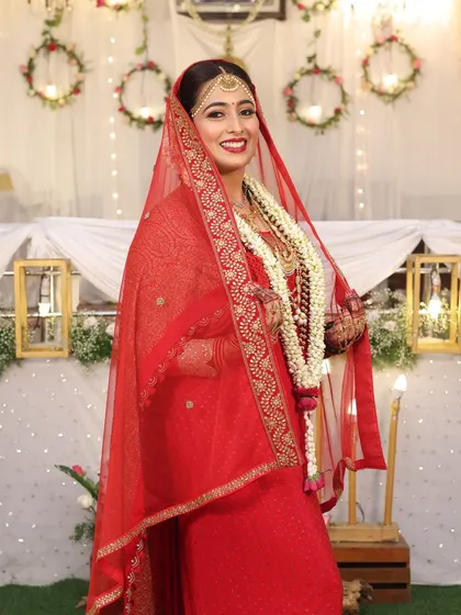 A full-length portrait of the bride, looking regal in her red saree and veil.