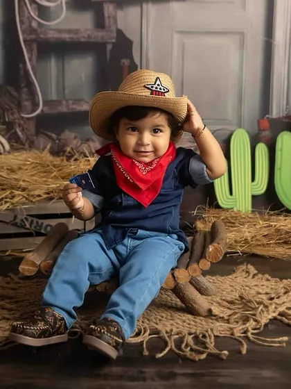 Tipping his hat like a true gentleman. The rustic barn backdrop completes this adorable cowboy theme.