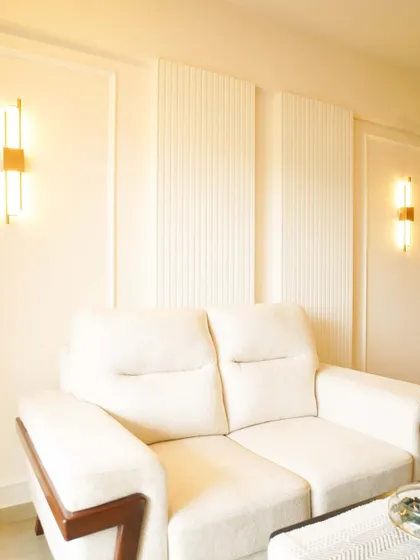 A cozy living room corner with a two-seater sofa set against a wall with fluted panels and classic molding. The warm lighting from the sconces creates an intimate atmosphere.