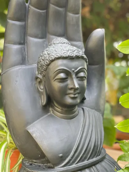 The dark, smooth finish of this black marble Buddha hand statue contrasts beautifully with the surrounding green foliage.