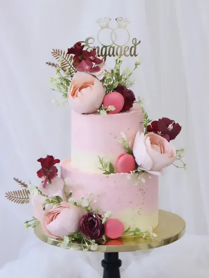 A beautiful two-tiered engagement cake featuring a soft pink and white ombre design. This romantic cake is decorated with fresh peonies and macarons, combining classic elegance with modern touches.