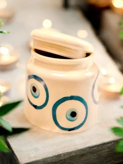 A charming ceramic jar with a lid, hand-painted with the evil eye design. It's perfect for storing trinkets or dry fruits and makes for a useful and sustainable gift.