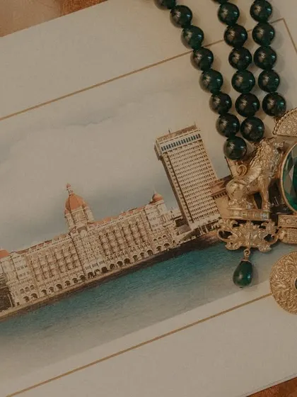 A detail shot of the wedding invitation and the bride's jewelry, set against the backdrop of the Taj Mahal Palace.