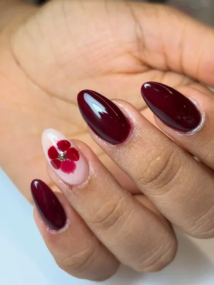 A close-up of the blooming berry bliss nail. The single accent nail features a beautiful flower made from real petals, set against the deep red polish.