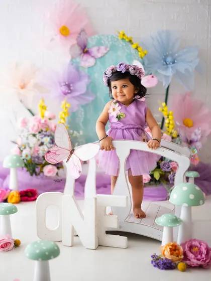 One year old and full of wonder! Standing on a bridge in a pastel fairy garden, this baby girl is celebrating her first birthday in the most enchanting way.