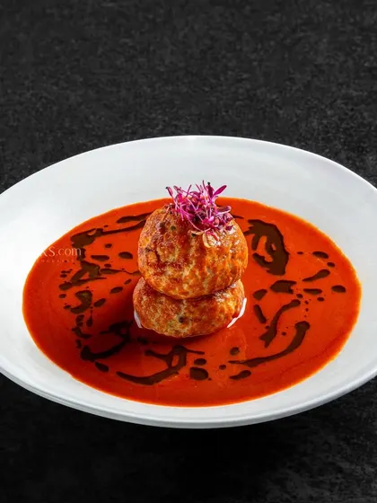 Chicken meatballs stacked in a spicy red curry, drizzled with a dark sauce for an artistic touch.