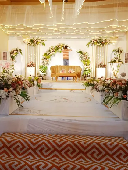This behind-the-scenes photo shows the scale of a wedding reception stage I was setting up in a hall. The design features a floral arch over the main sofa and multiple floral arrangements on pedestals.