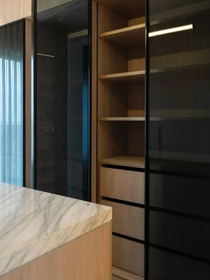 The combination of dark tinted glass doors and warm wood interiors creates a sophisticated and modern look for this wardrobe. The glass offers a subtle glimpse of the contents while maintaining a sleek, clean aesthetic.