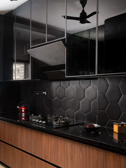 We designed this sleek, modern kitchen with dark wood base cabinets, black hexagonal tiles, and reflective black upper cabinets that cleverly conceal the chimney.