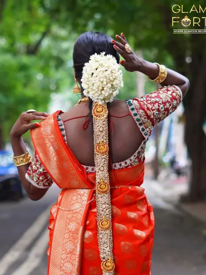 The back view of a traditional South Indian bridal hairstyle. The long braid is adorned with golden accessories and fresh jasmine flowers, creating a truly iconic and elegant look.