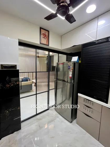 A view of a modern kitchen with a glass partition separating it from the living area. The kitchen features a mix of white and beige cabinets, with a black roller shutter for appliances.