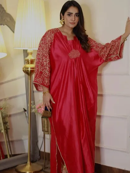 A vibrant red kaftan with gold embroidered sleeves. This comfortable yet glamorous piece is perfect for a festive evening at home or a relaxed celebration with friends.