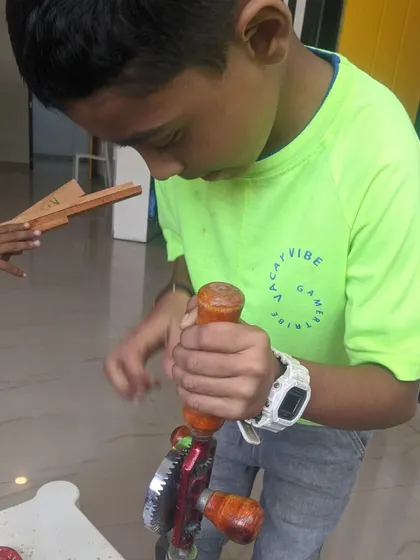 This student is learning the clockwise motion needed to operate a manual hand drill, a key lesson in simple mechanics.