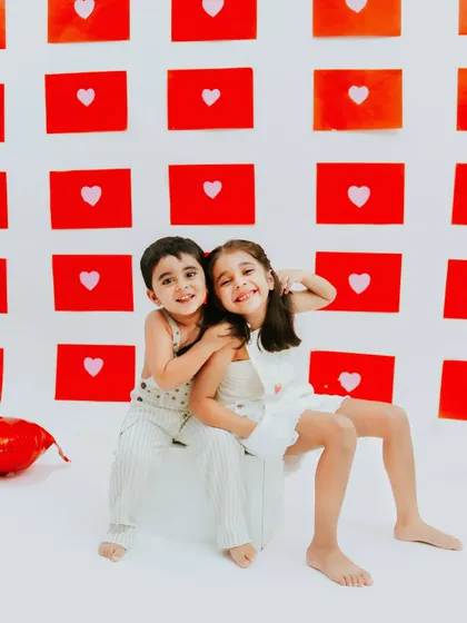 A sweet hug and a shared smile. The simple red heart background adds a pop of color and love to this sibling photoshoot.