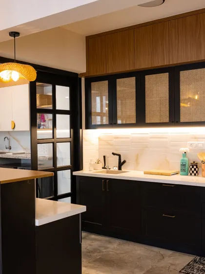 This kitchen showcases a sleek, modern aesthetic with black cabinets, a white marble backsplash, and rattan-front upper cabinets. The breakfast bar and pendant light complete this stylish and functional space.
