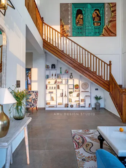 A view of the grand staircase and living area in 'The Mountain Home.' We designed a custom bookshelf to fit perfectly under the stairs, maximizing storage and creating a beautiful architectural feature.