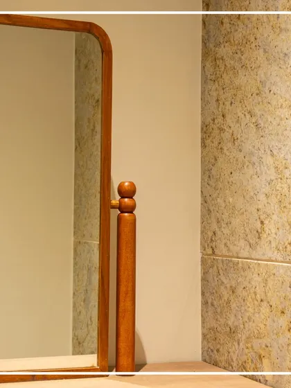 A close-up view highlights the rich texture of the colonial gold stone wall panels and the custom wooden frame of the mirror. The turned wood detail on the mirror's pivot mechanism is a small nod to traditional craftsmanship.