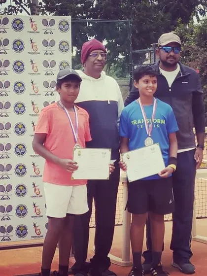 Two junior boys display their medals and certificates after competing in the AITA TS7 U-14 tournament.