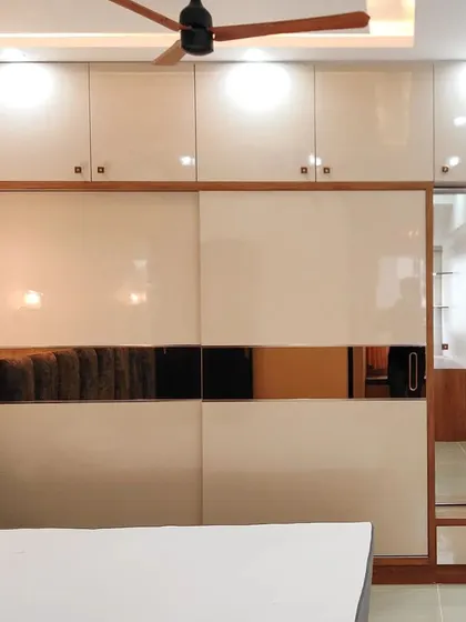 This sliding wardrobe combines off-white glossy panels with a central band of tinted mirror, which helps to make the room feel larger and brighter. The design includes an integrated dressing table with open shelves.
