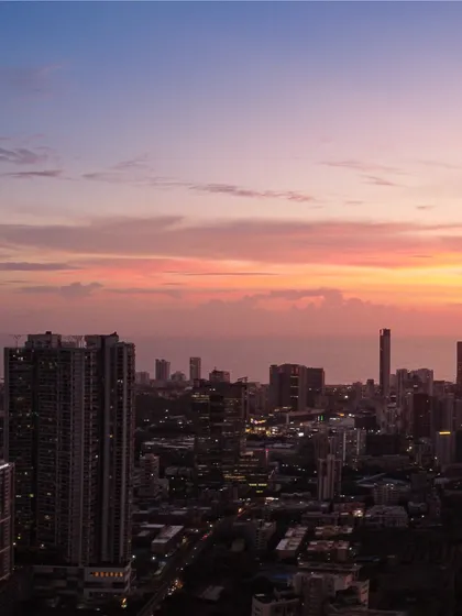 A close-up view of Mumbai's coastal buildings at dusk, with the sky showing soft hues of pink and orange after sunset.