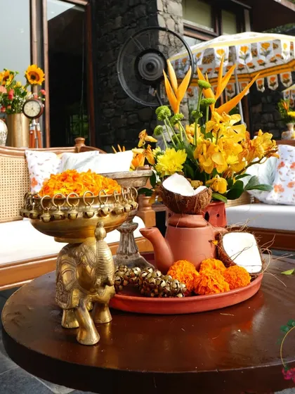 A Haldi ceremony detail, with a brass elephant bowl filled with marigold petals on a rustic wooden table.