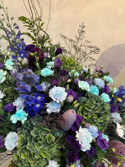 A close-up of an immaculate and incredibly chic arrangement. The juxtaposition of sea-green carnations against deep purple and blue flowers creates a stunning and harmonious color story.