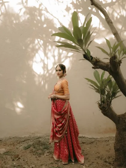 A bride stands gracefully near a tree, the shadows and light playing on the wall behind her.