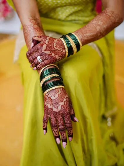 A close-up of the bride's hands, displaying her henna and traditional green bangles.