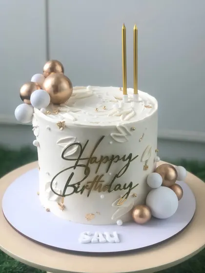 Another view of the white and gold birthday cake, showing the subtle texture and placement of the decorations.