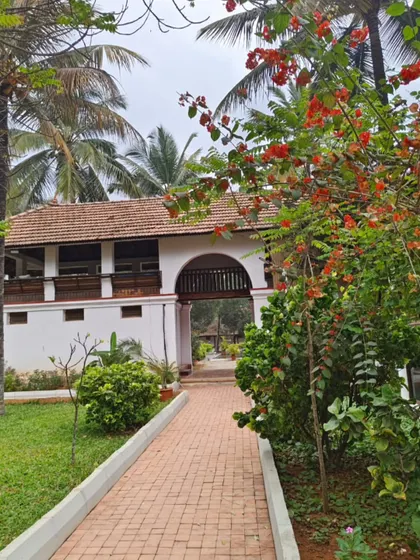 A pathway leading to the Padipura, framed by red bougainvillea and palm trees. This heritage structure serves as a gateway to a space of silence and inner peace.