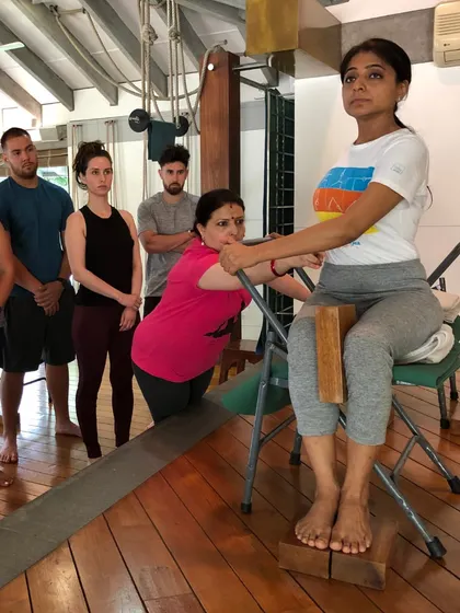 Students are being guided in a supported forward bend. You can see the focused attention and hands-on adjustments that ensure each person is working correctly and safely.
