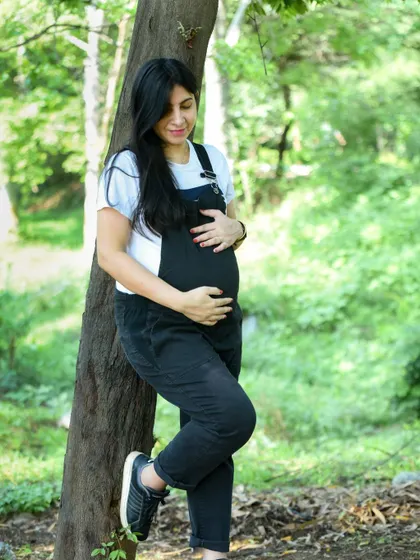 A quiet, contemplative moment for this mom-to-be, dressed in casual black dungarees while leaning against a tree in a park.