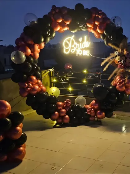 This circular balloon arch in black and metallic red makes a bold statement for a "Bride to be" party backdrop.