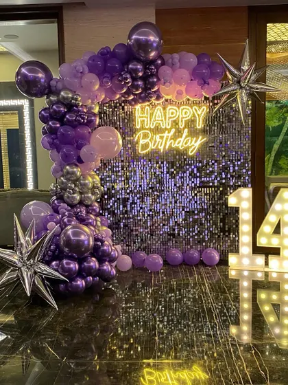 This is a duplicate of ID 64, 115, 129, 159, 196. A glamorous 14th birthday setup with a purple shimmer wall. This decoration features a stunning organic balloon garland in shades of purple and silver, a 'Happy Birthday' neon sign, and large marquee numbers.