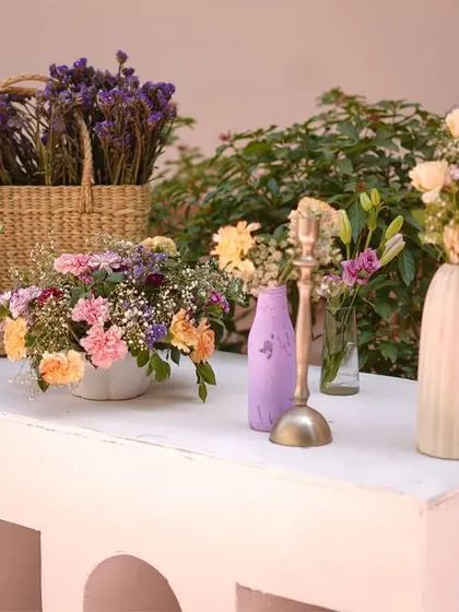A beautiful floral arrangement on a modern white console. The mix of flowers in vases and a woven basket adds texture and a touch of rustic charm to the pastel theme.