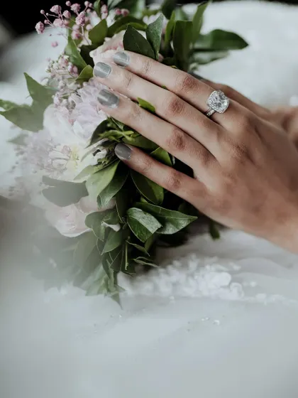 A close-up on the bride's hands, showcasing her stunning engagement ring as she holds her bouquet.