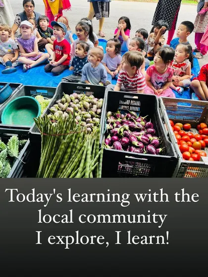 A group of children sits attentively at a local vegetable stall, a perfect example of experiential learning within our community.