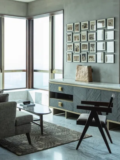 A seating area within the master bedroom, featuring a chair by Mahendra Doshi and a custom console in stone veneer and brass. The wall displays a grid of personal photographs, adding a layer of warmth and history.