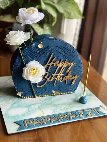 Less is more with this minimal yet striking half-moon cake. The deep blue textured design with white floral accents was created for a "Paparazzi" themed birthday.