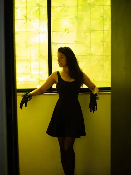 A full-body shot in a little black dress, posed in a yellow-tinted doorway to create a dramatic, high-contrast look.