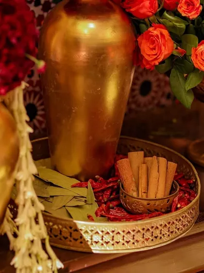 A detail shot of a decorative tray with cinnamon sticks and bay leaves, placed next to golden vases of red and orange roses. This highlights the thoughtful combination of floral and symbolic elements.