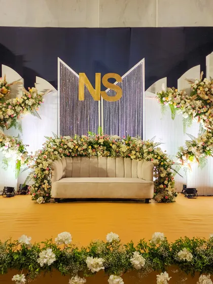 A wider perspective of the 'NS' monogram stage, showing how the elements come together. The design features a navy blue backdrop, white paneled wings, and asymmetrical floral arrangements for a contemporary yet balanced look.