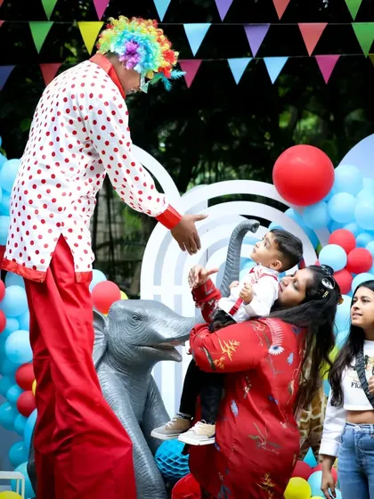 A stilt-walking clown greets the birthday boy and his mother, adding a touch of spectacle and wonder to the event.